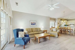 Ein geräumiges Wohnzimmer mit Sofa, Sesseln und Couchtisch, ein Essbereich mit Stühlen und eine Küche im Hintergrund.