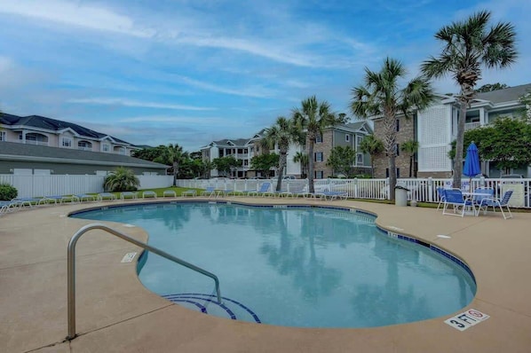 A swimming pool with a poolside area, palm trees, and a white fence. - Magnolia Pointe Unit 305 (Myrtle Beach)