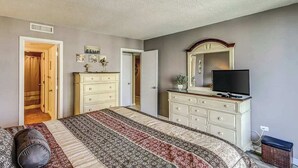 Een slaapkamer met een bed, een dressoir, een televisie en een deur die naar een andere kamer leidt.