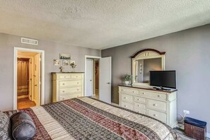 A bedroom with a bed, dresser, television, and a door leading to another room. - Ocean Creek Plantation DD-6 (Myrtle Beach)