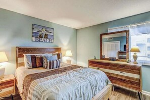 Un dormitorio con cama, mesitas de noche, cómoda, espejo y una obra de arte en la pared.