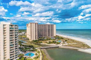 Un hotel frente al mar con varios edificios altos, una playa y una piscina.