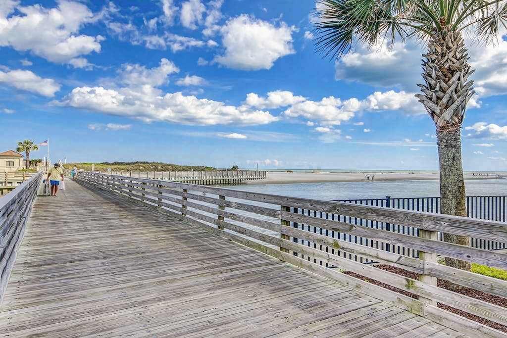 A wooden boardwalk leading to a beach with a palm tree on the right.