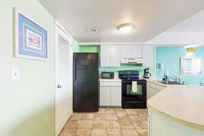 A compact kitchen with a refrigerator, microwave, oven, and a sink. - Palace Resort Unit 813 (Myrtle Beach)