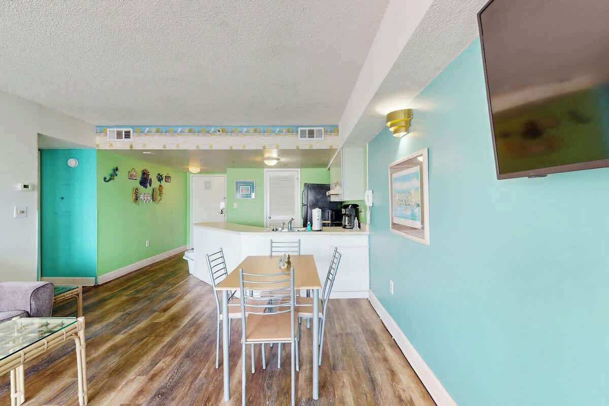 A dining area with a table and chairs, a kitchen area with appliances, and a living space with a television.