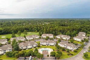 Un quartier résidentiel composé de plusieurs maisons à deux étages, avec une piscine centrale et, au loin, un terrain de golf.