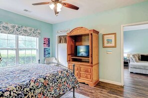 A bedroom with a bed, a wooden TV stand, a ceiling fan, and a window with blinds. - Legends Resort - Montrose C (Myrtle Beach)