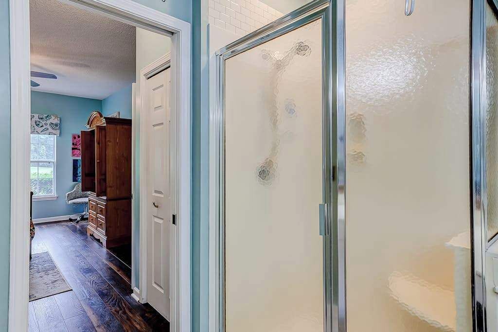 A hallway with a wooden floor, a white door, and a glass shower enclosure.