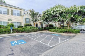 A parking area with handicapped parking spaces, a building with a sign, and a tree-lined street. - Legends Resort - Montrose C (Myrtle Beach)