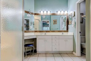 Une salle de bain avec un grand miroir, deux lavabos, un meuble-lavabo et une chaise.
