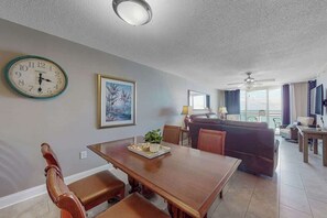 A dining area with a wooden table and benches, a clock on the wall, and a painting. - Bahama Sands Unit 0706 (North Myrtle Beach)