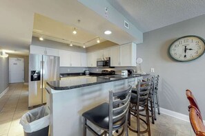 A modern kitchen with a central island, stainless steel appliances, and a clock on the wall. - Bahama Sands Unit 0706 (North Myrtle Beach)