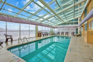 An indoor swimming pool with clear glass ceilings, lounge chairs, and a view of the city. - Bahama Sands Unit 0706 (North Myrtle Beach)