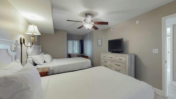 Quarto de hotel com duas camas, um ventilador de teto, uma televisão e um armário.