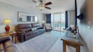 Quarto de hotel com sofá de couro, uma mesinha, televisão e varanda com vista.