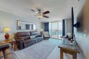 A hotel room with a leather sofa, a small table, a TV, and a balcony with a view. - Bahama Sands Unit 0706 (North Myrtle Beach)