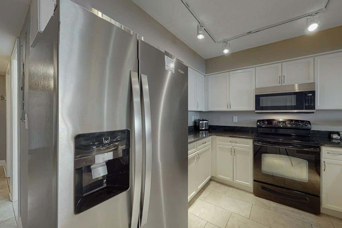 A modern kitchen with stainless steel appliances, white cabinetry, and a tiled floor.