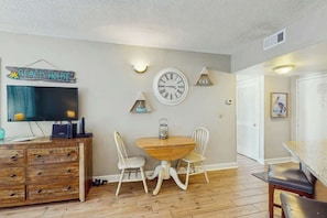 A living room with a TV, wooden cabinet, dining table, and chairs. - Palace Resort Unit 1210 (Myrtle Beach)