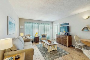 A living room with a sofa, coffee table, TV, and a wooden cabinet. - Palace Resort Unit 1210 (Myrtle Beach)