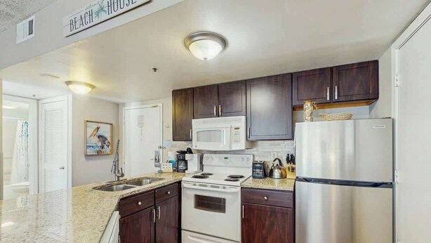 Una cocina con armarios de madera oscura, estufa blanca, microondas y refrigerador de acero inoxidable.
