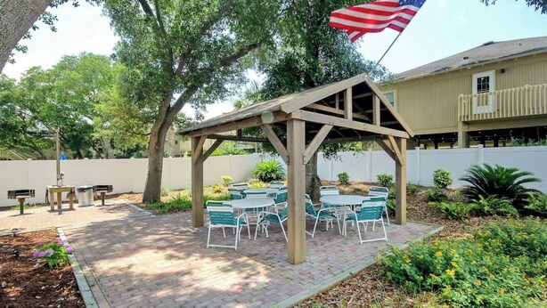 An outdoor patio with a wooden pergola, green metal chairs, and a flag. - Pelicans Watch Unit 121 (Myrtle Beach)