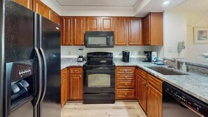 A kitchen with wooden cabinets, a black refrigerator, a microwave, a stove, and a dishwasher. - Pelicans Watch Unit 121 (Myrtle Beach)