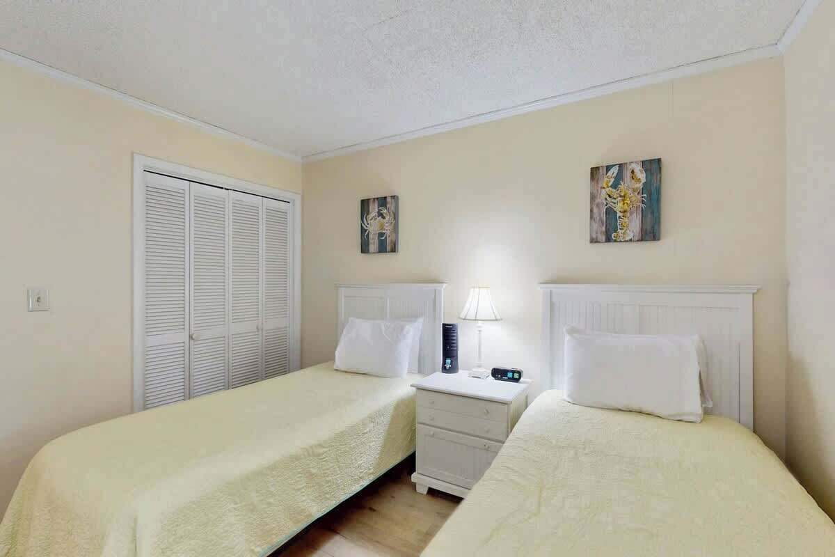 A hotel room with two beds, a nightstand, a lamp, and a closet.