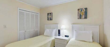 A hotel room with two beds, a nightstand, a lamp, and a closet.