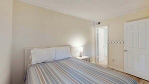 A bedroom with a bed, bedside lamp, and a door with a coat rack. - Pelicans Watch Unit 121 (Myrtle Beach)