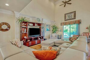 A living room with a sectional sofa, a flat-screen TV, decorative shelves, and a ceiling fan. - K & K Getaway Retreat (Atlantic Beach)