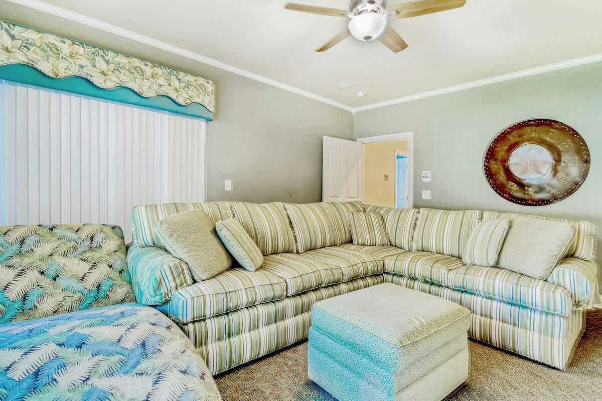 Ein Wohnzimmer mit einem gestreiften Ecksofa, einem passenden Hocker, einem Deckenventilator und einer Wandplatte.