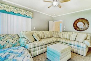 Ein Wohnzimmer mit einem gestreiften Ecksofa, einem passenden Hocker, einem Deckenventilator und einer Wandplatte.