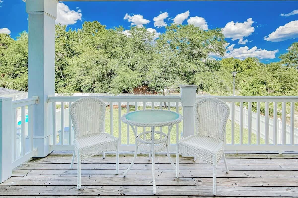 A covered outdoor area with a white railing, two wicker chairs, and a small round table.