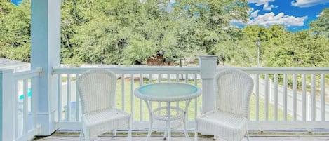 A covered outdoor area with a white railing, two wicker chairs, and a small round table.