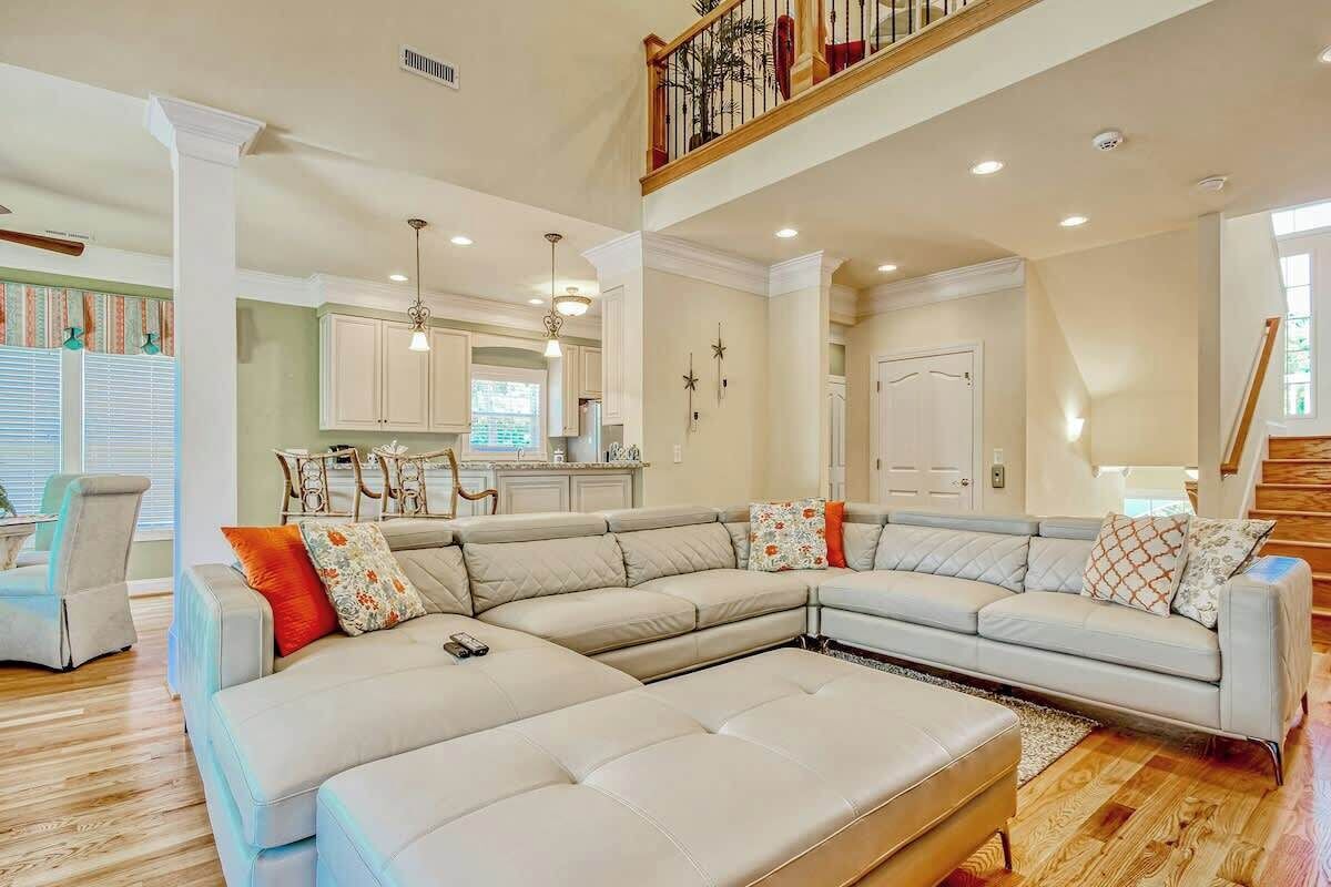 A spacious living area with a sectional sofa, a dining table, and a kitchen in the background.