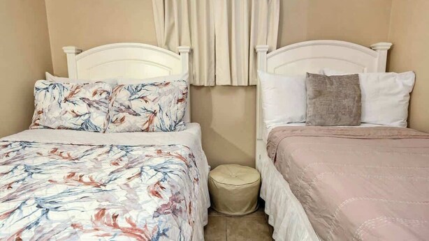 A bedroom with two beds, each with a different style of bedding. There is a small round ottoman between the beds. - Myrtle Beach Resort B-349 (Myrtle Beach)