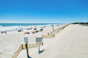Ein Strand mit einer Holzbrüstung, Strandbesuchern und einem klaren Himmel.