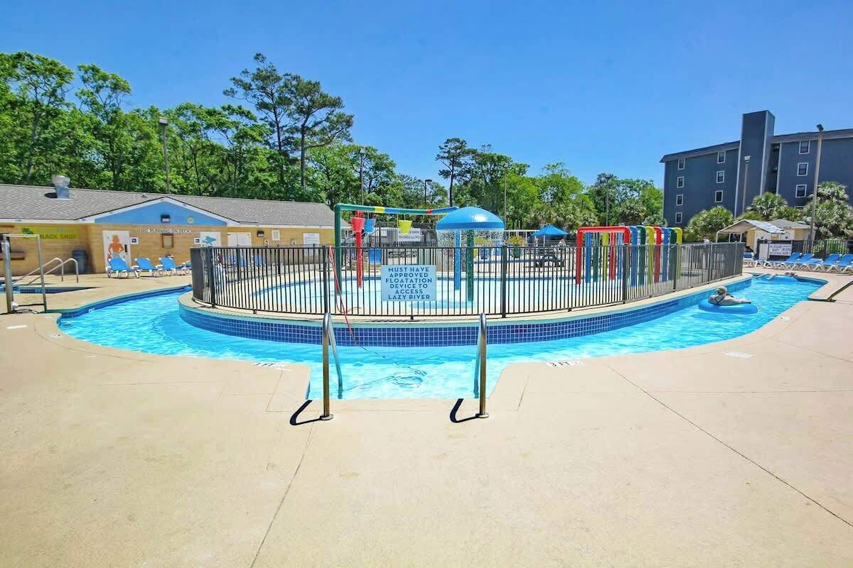 Una piscina amb una zona de jocs tancada per una tanca, un tobogan aquàtic i un altà de socorristes.