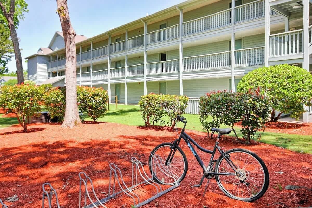 A multi-story building with balconies, a bicycle parked in front, and a red mulch ground cover.