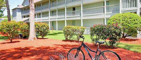 A multi-story building with balconies, a bicycle parked in front, and a red mulch ground cover.
