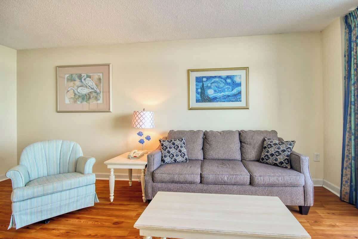 A living room with a sofa, armchair, and a coffee table. There are two framed artworks on the wall.