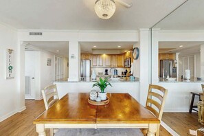 A dining area with a wooden table, chairs, a chandelier, and a kitchen in the background. - Ocean Creek Plantation D-1 (Myrtle Beach)