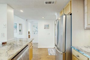 A modern kitchen with a stainless steel refrigerator, wooden cabinets, and a marble countertop. - Ocean Creek Plantation D-1 (Myrtle Beach)