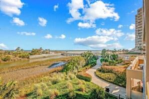 A coastal landscape with a pathway, a bridge, and a building with balconies. - Ocean Creek Plantation D-1 (Myrtle Beach)