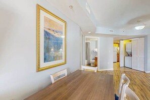 A dining area with a wooden table and chairs, a framed painting on the wall, and a view into the kitchen area. - Ocean Reef Resort 723 (Myrtle Beach)