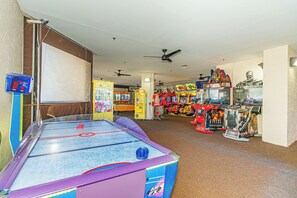 A room with a shuffleboard table, arcade games, and a large screen TV. - Ocean Reef Resort 723 (Myrtle Beach)