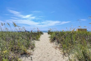 A sandy beach path flanked by tall grass leading to the sea, with beach umbrellas and a few people in the distance. - Atlantica Resort PH51 (Myrtle Beach)