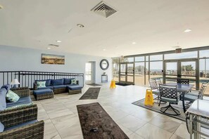A spacious indoor area with a seating arrangement, a large window offering a view, and a circular wall decoration. - Atlantica Resort PH51 (Myrtle Beach)