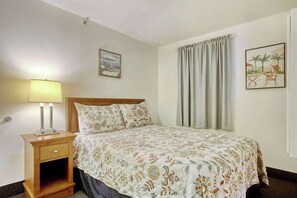A hotel room with a bed, a nightstand with a lamp, a window with curtains, and two wall art pieces. - Atlantica Resort PH51 (Myrtle Beach)