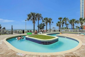 A pool area with a clear view of the ocean, palm trees, and a building in the background. - Atlantica Resort PH51 (Myrtle Beach)